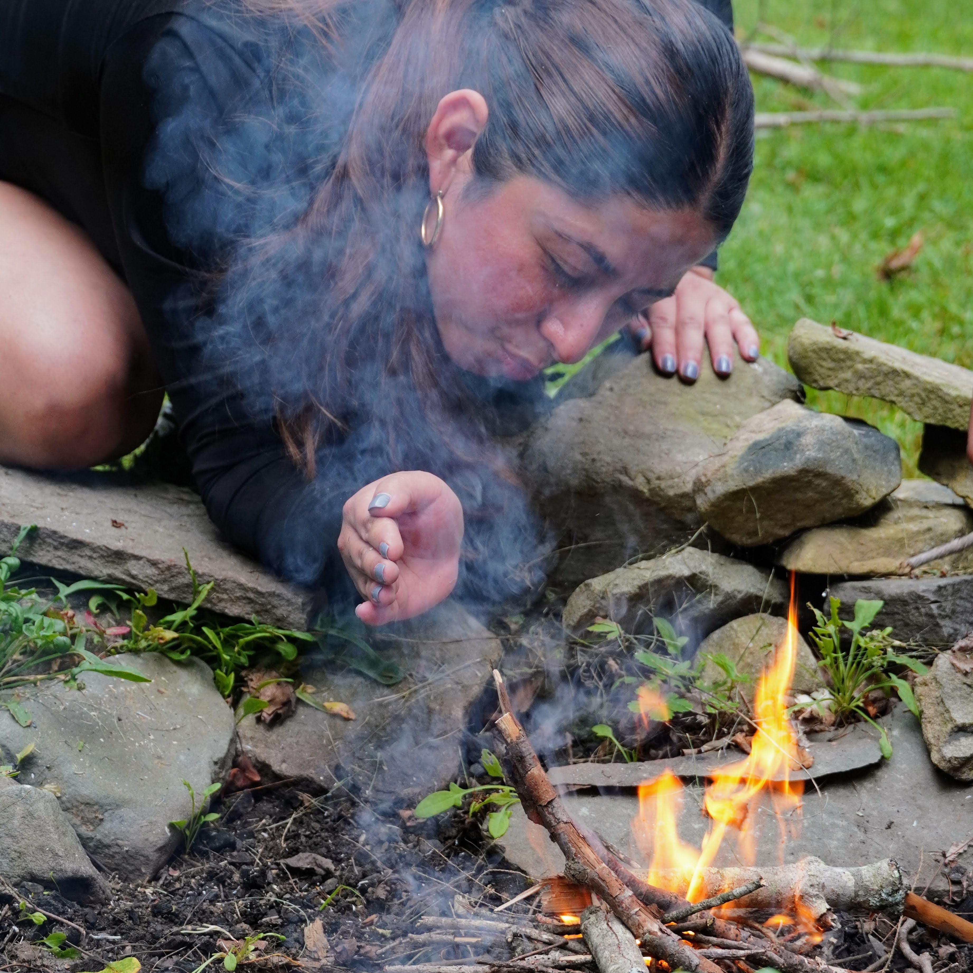 Person lying on rocks by a small campfire with smoke rising