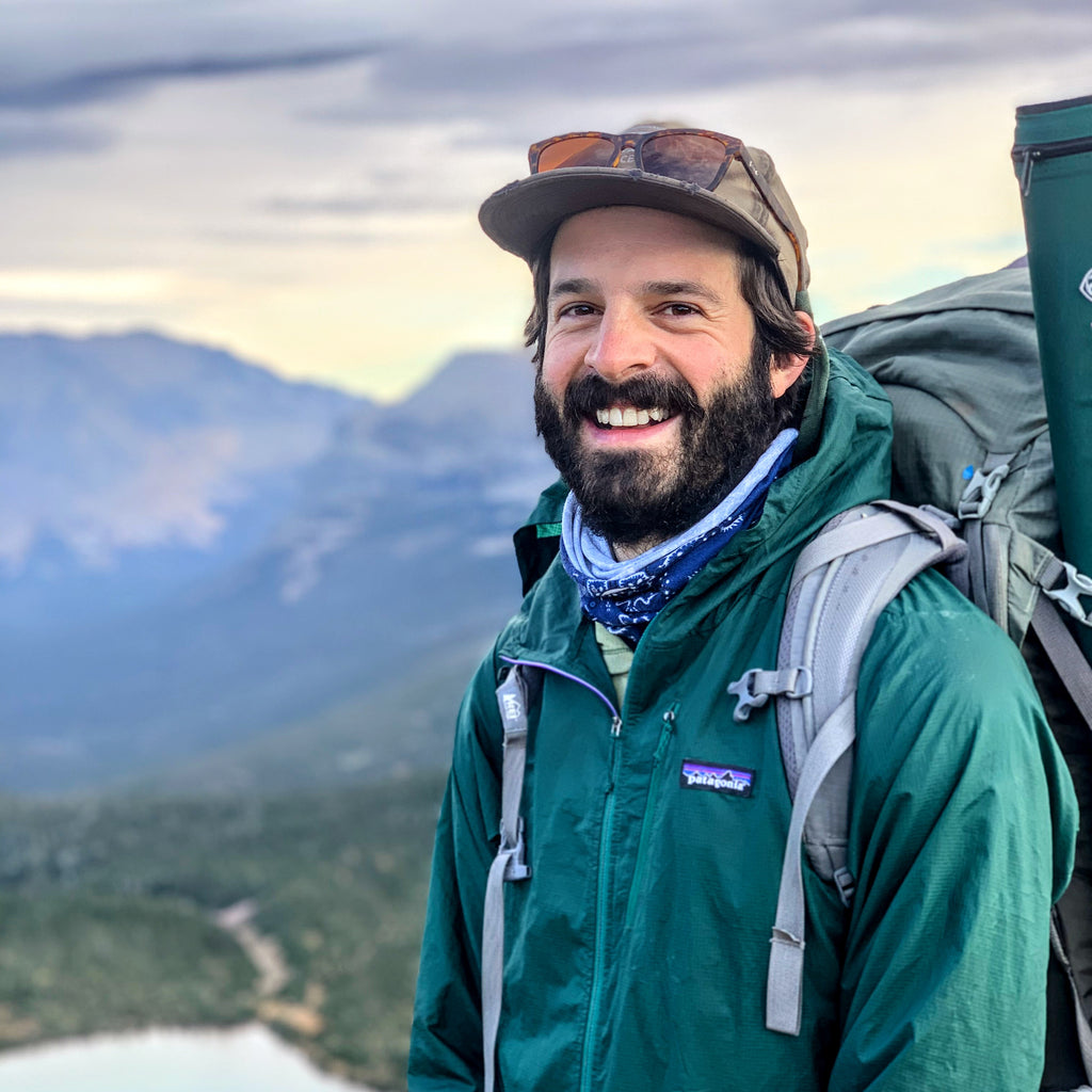 apprentice guide devin o'brien poses in front of a mountain vista with a backpack on