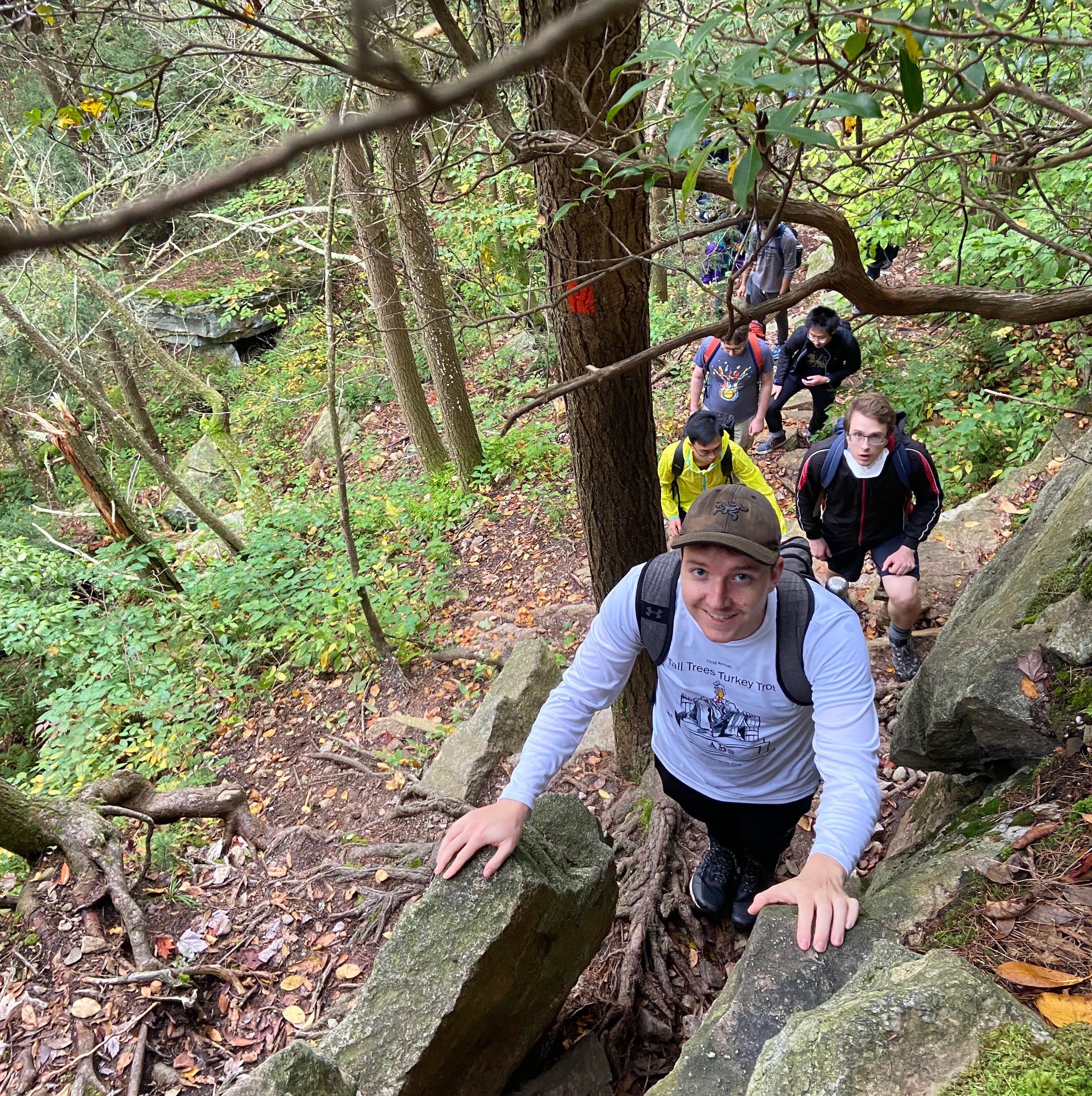 a person hikes up a rocky ledge with a group of hikers behind them