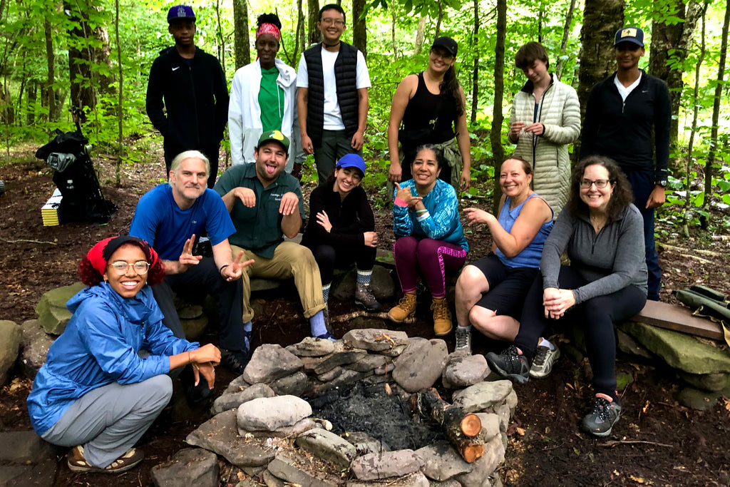 a group of backpackers gathered around a stone firepit in the woods