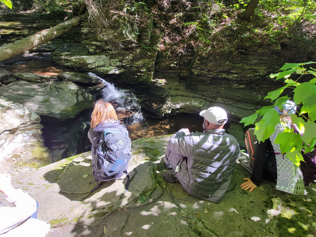 three hikers pause on a rock to admire a small backcountry waterfall