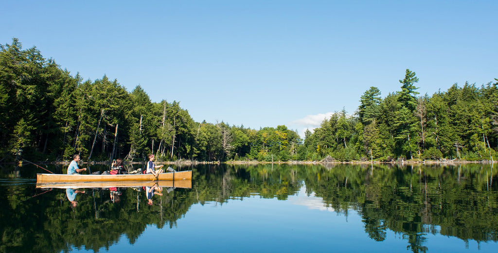 three people in a canoe on a crystal clear Adirondack lake in the summer
