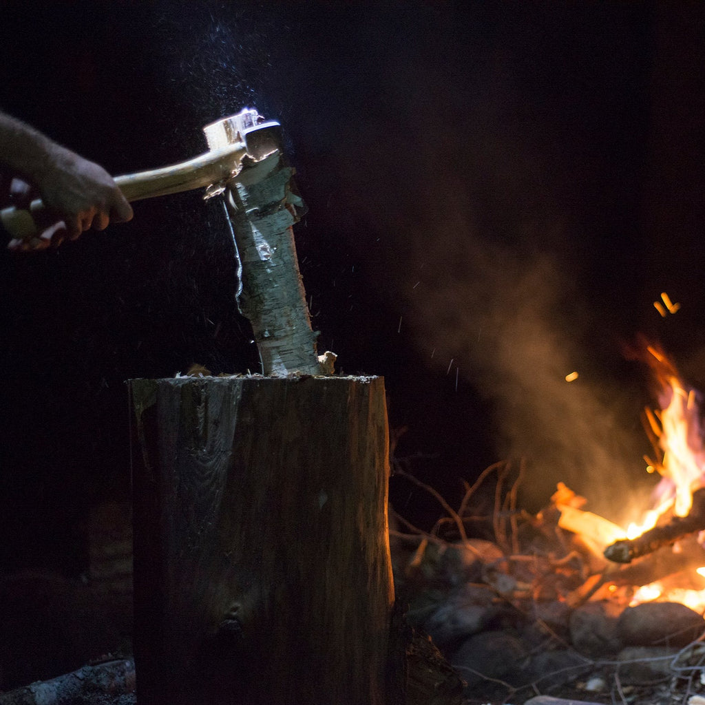 a person chopping wood on a block next to a roaring fire