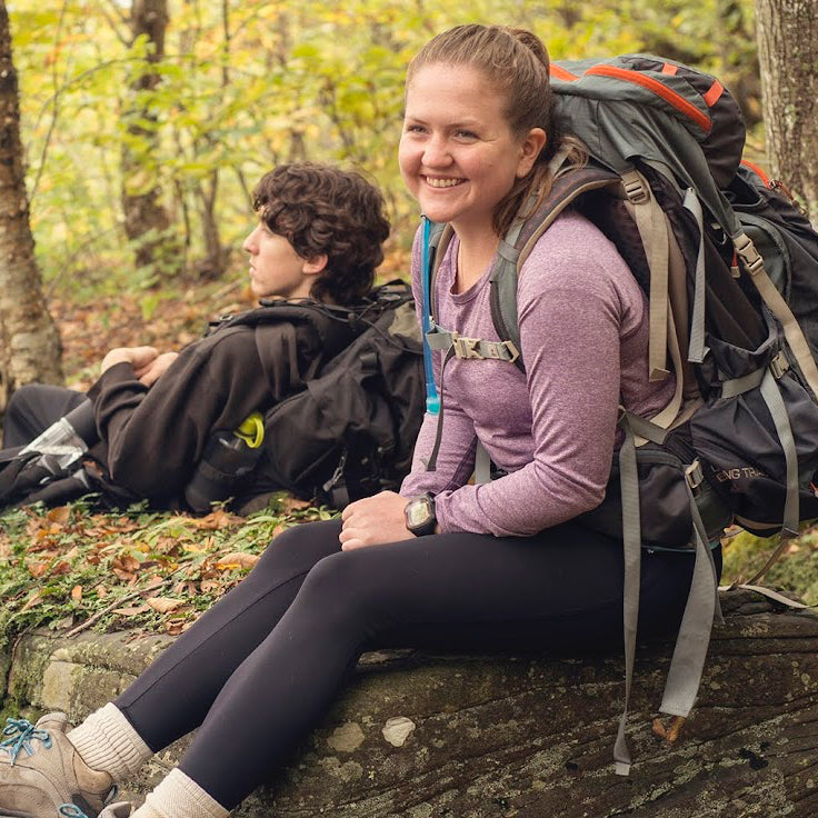 Two hikers with backpacks sitting on a rock in a forest