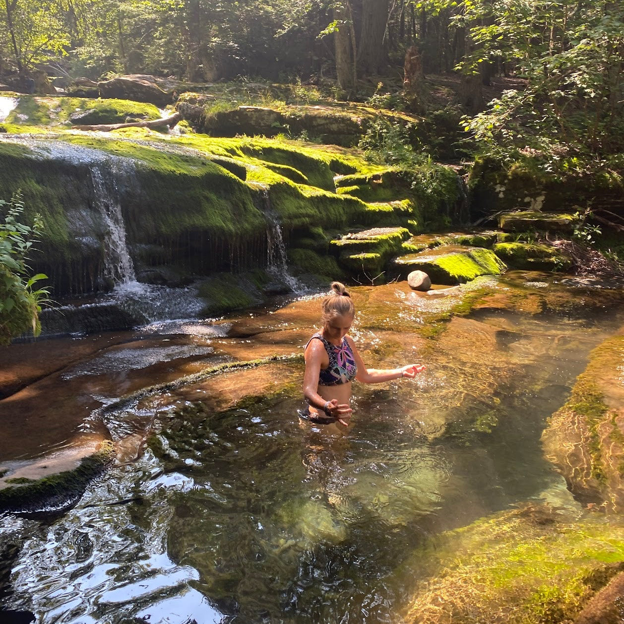 Person in a natural setting with a waterfall and greenery