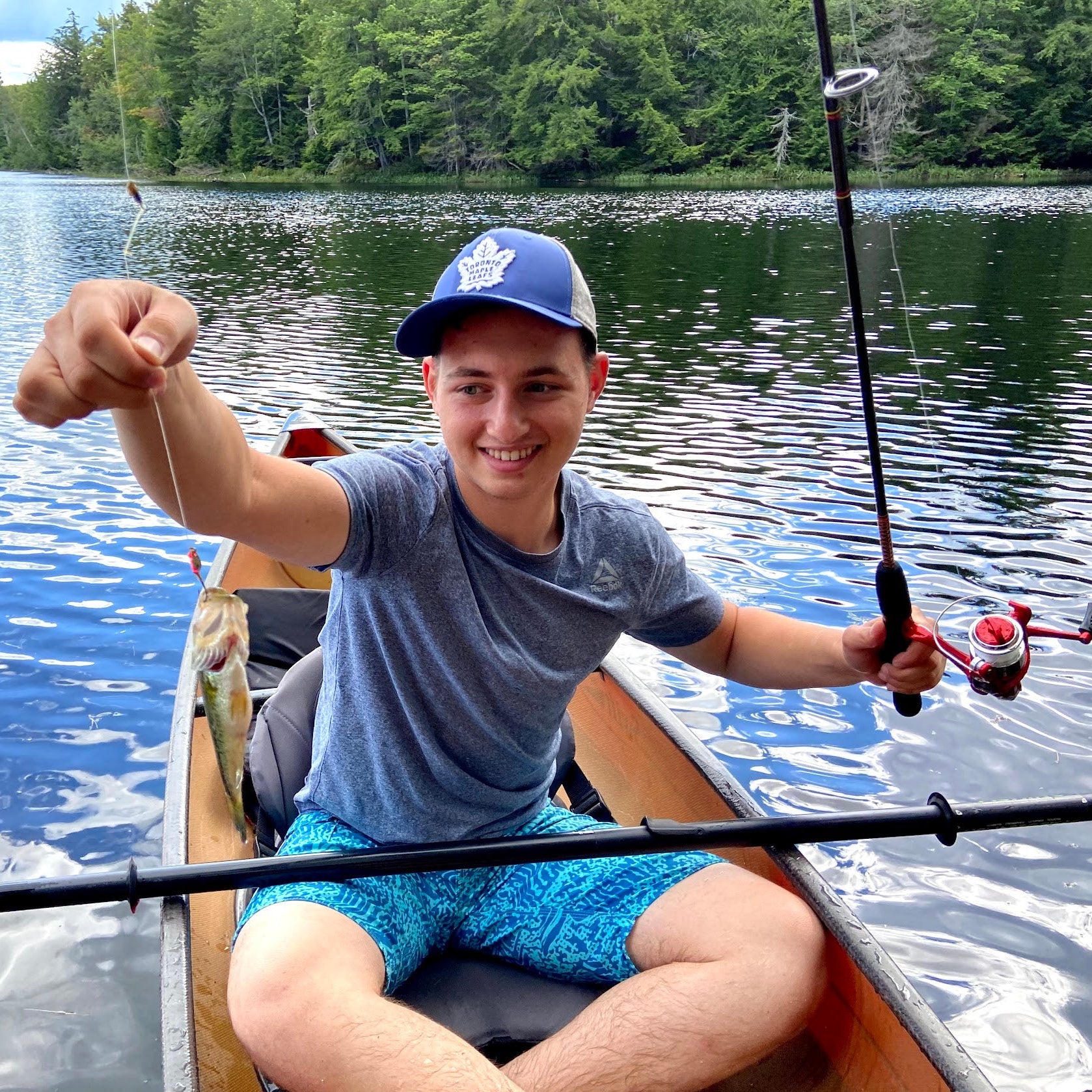 Person in a kayak on a lake holding a fishing rod, surrounded by trees.