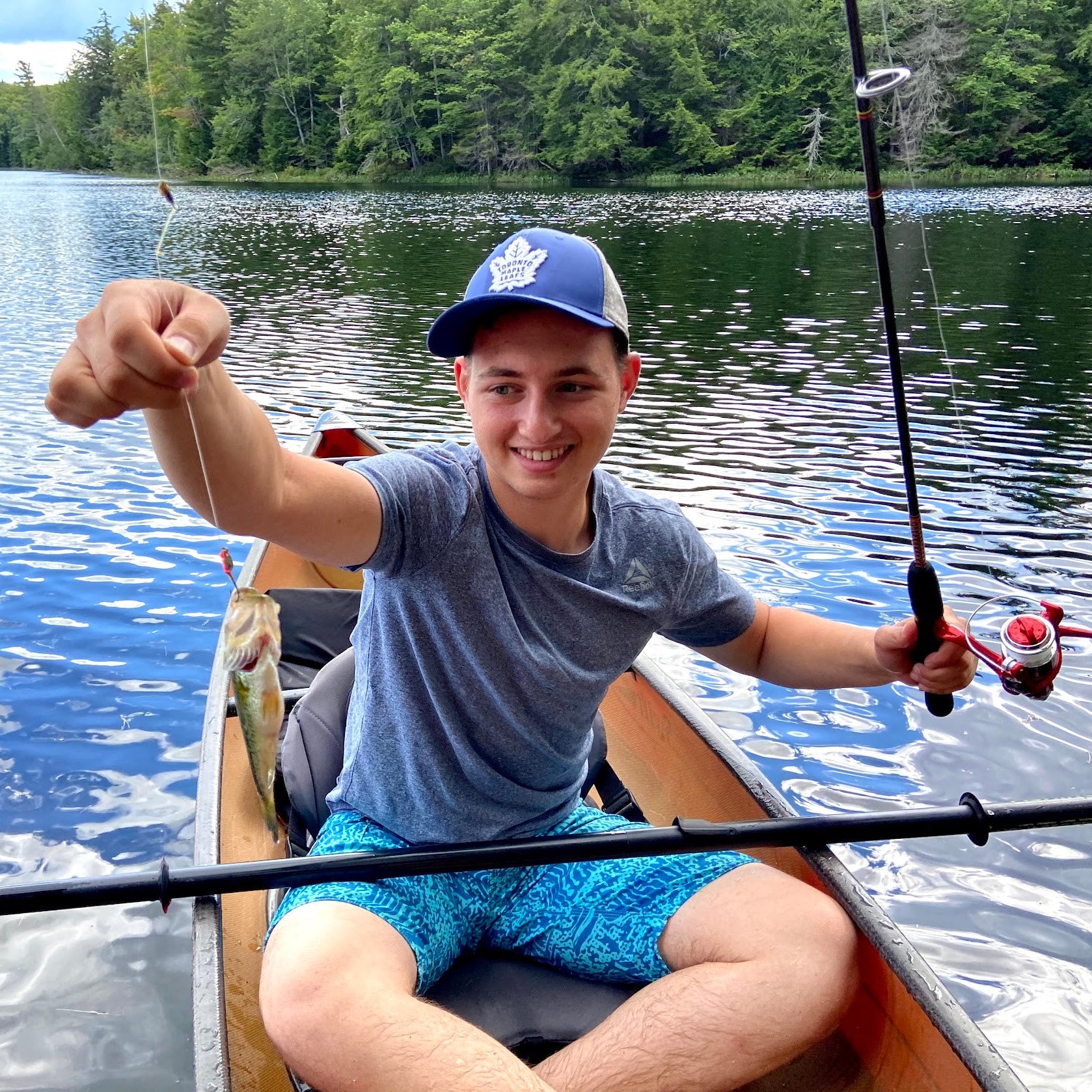 Person in a kayak on a lake holding a fishing rod, surrounded by trees