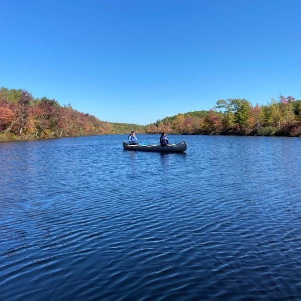 a canoe on a rippling lake with fall foliage in the background