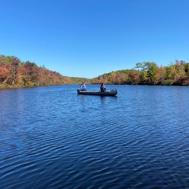 a canoe on a rippling lake with fall foliage in the background