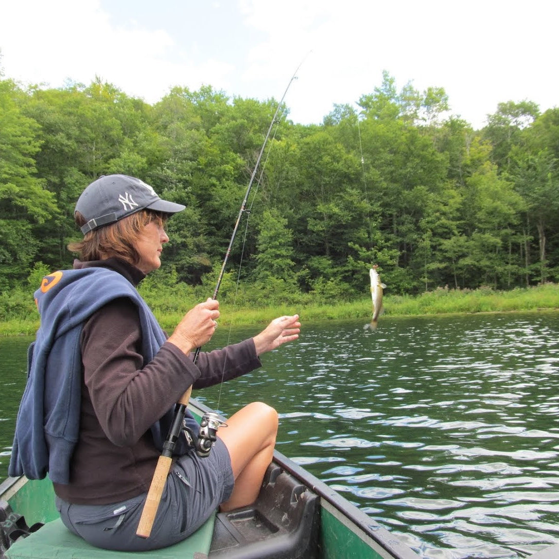 Person fishing from a canoe on a calm lake with trees in the background