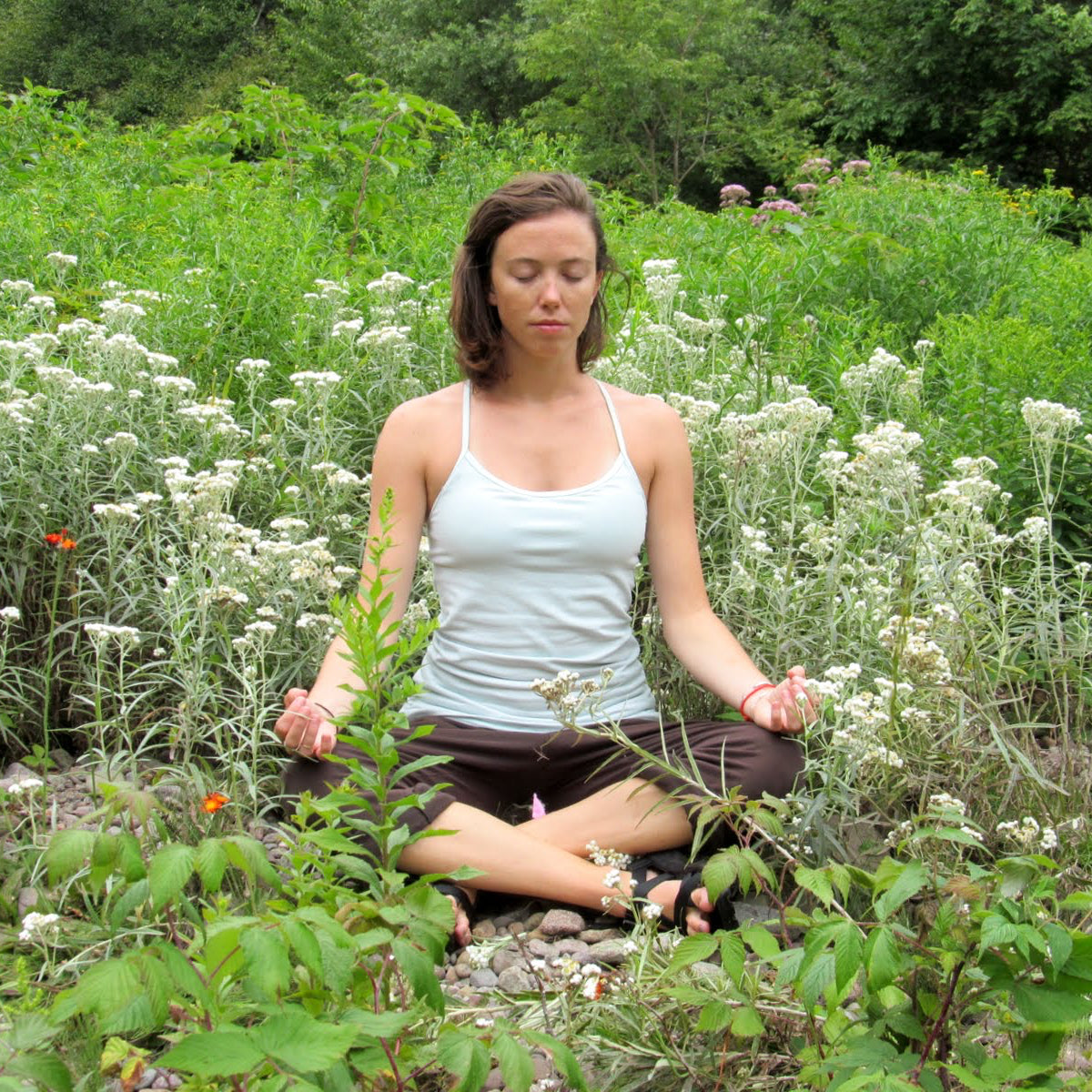 Woman meditating in a field of white flowers and greenery