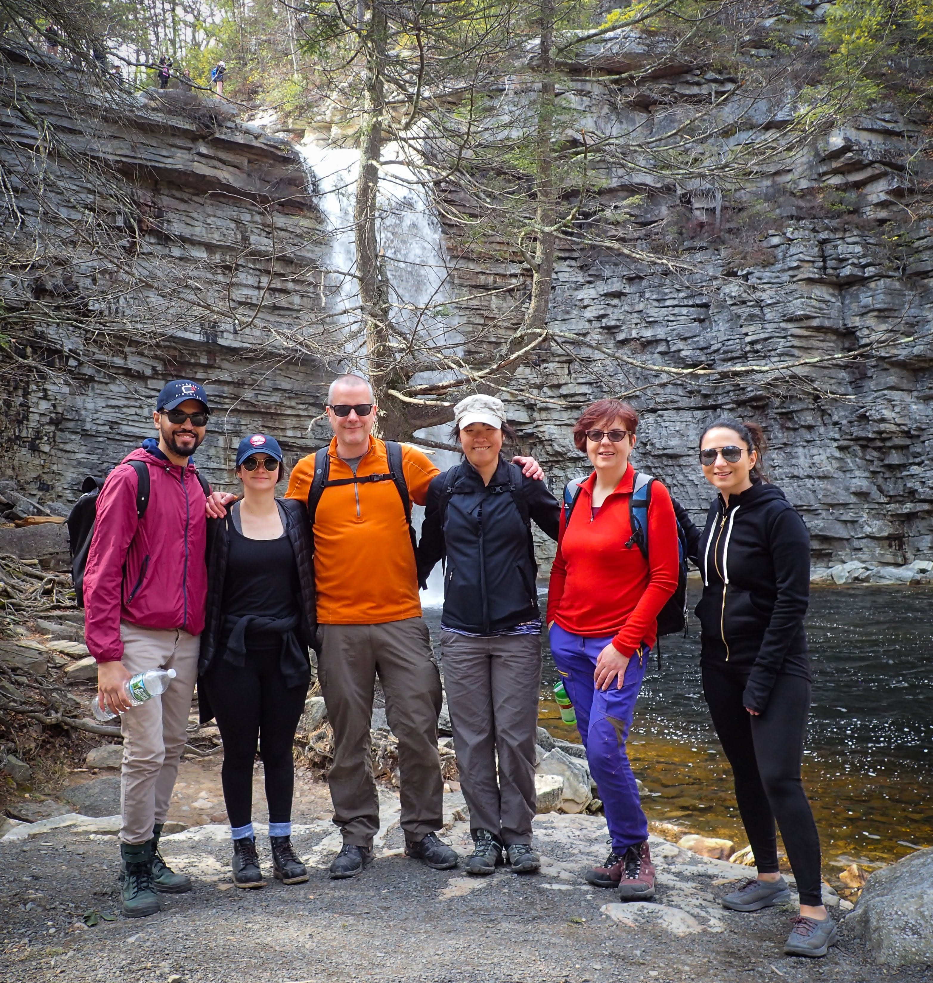 Group of six people posing for a photo in front of a waterfall.