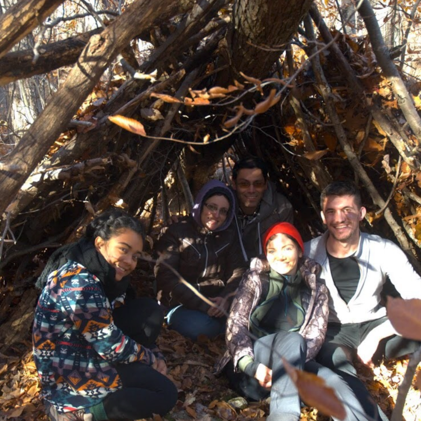 five people post in a debris shelter they built in the woods