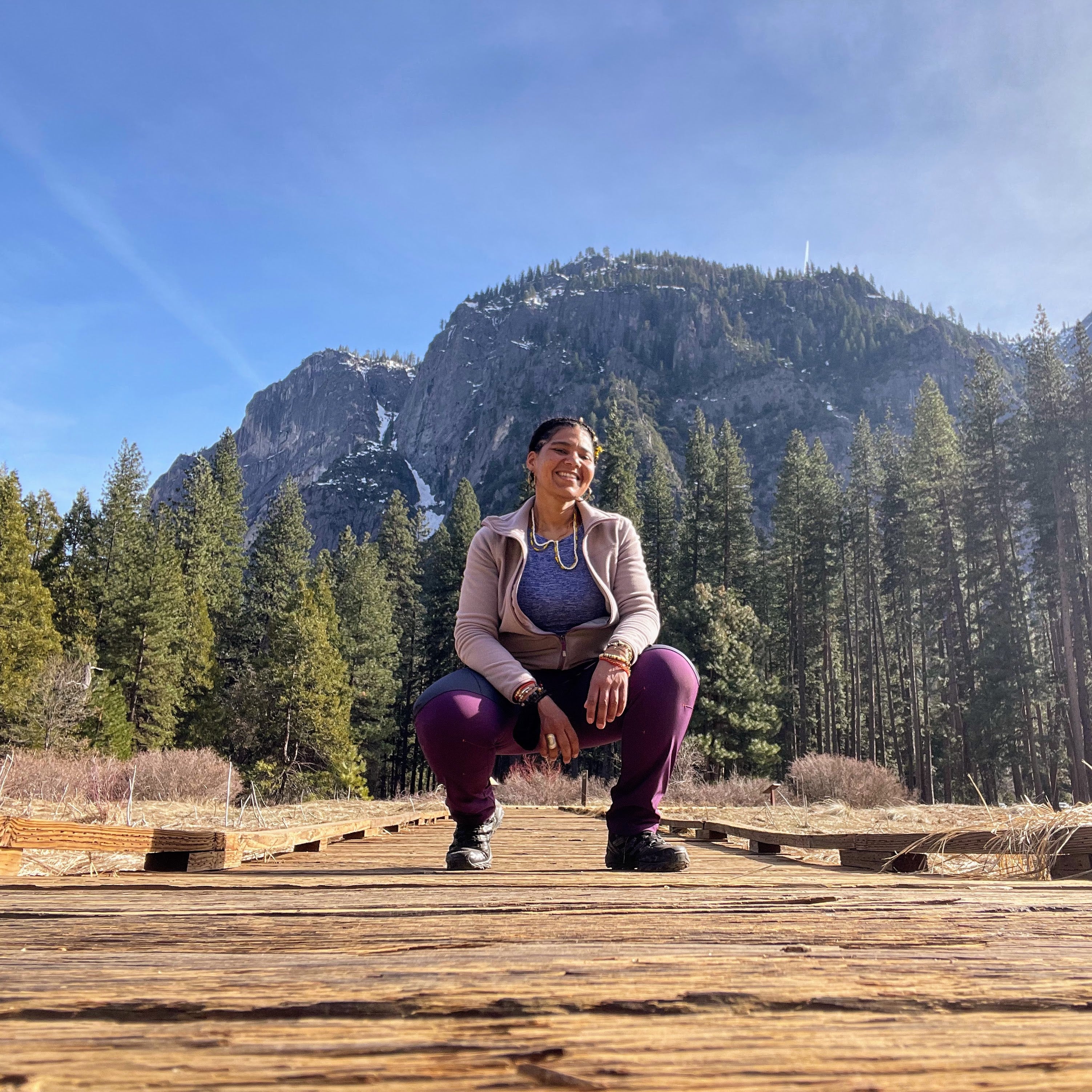 photo of lead guide Jenna Valette posing on trail in front of a mountain range and tall conifer trees