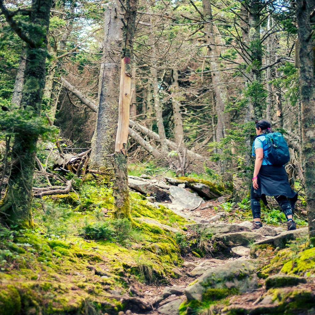 a hiker heads up a steep section of rocky trail with moss in the foreground