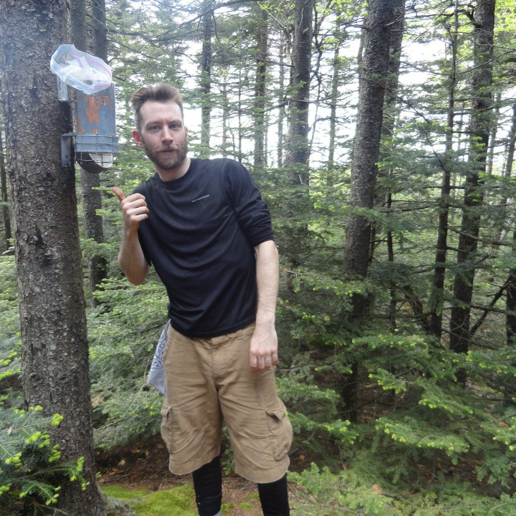 a hiker poses in front of a cannister at the top of a trail-less summit in the catskills