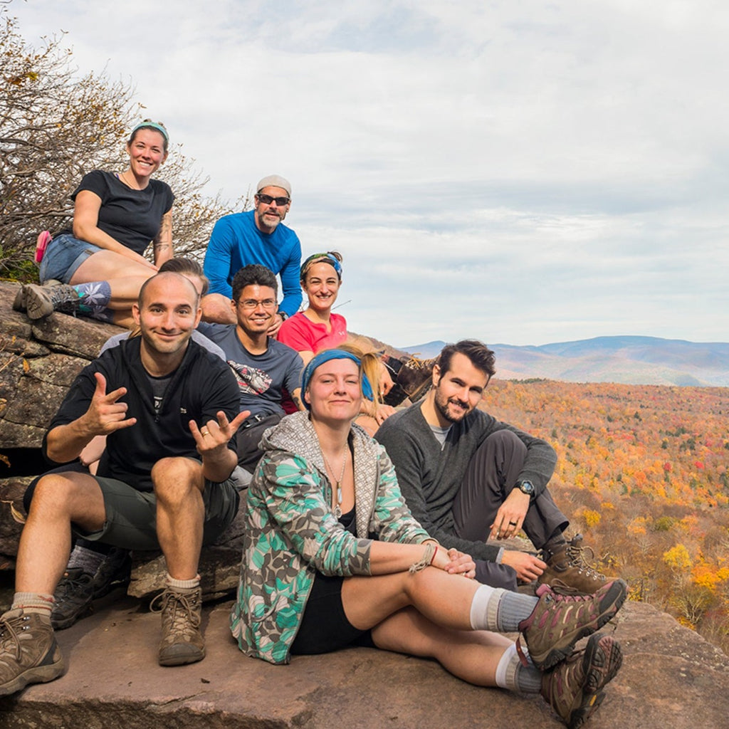 a group of hikers pose on giant ledge with the fall foliage over the catskills in the background