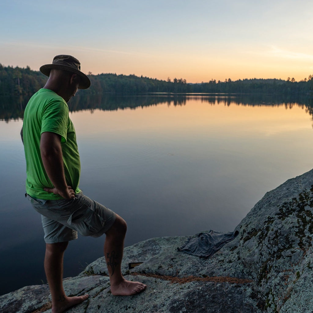 a person stands on a rock on the edge of an adirondack pond at duck