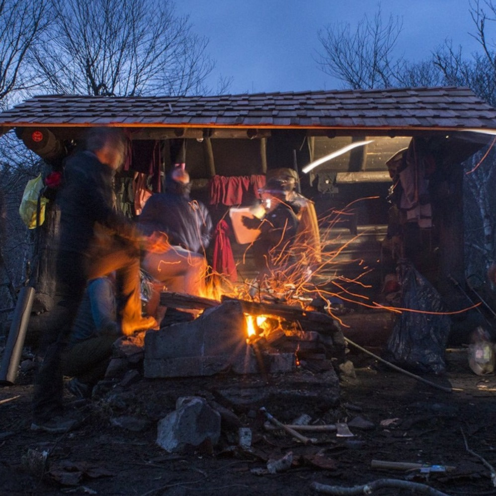 campers outside a leanto around a fire pit with a campfire at dusk